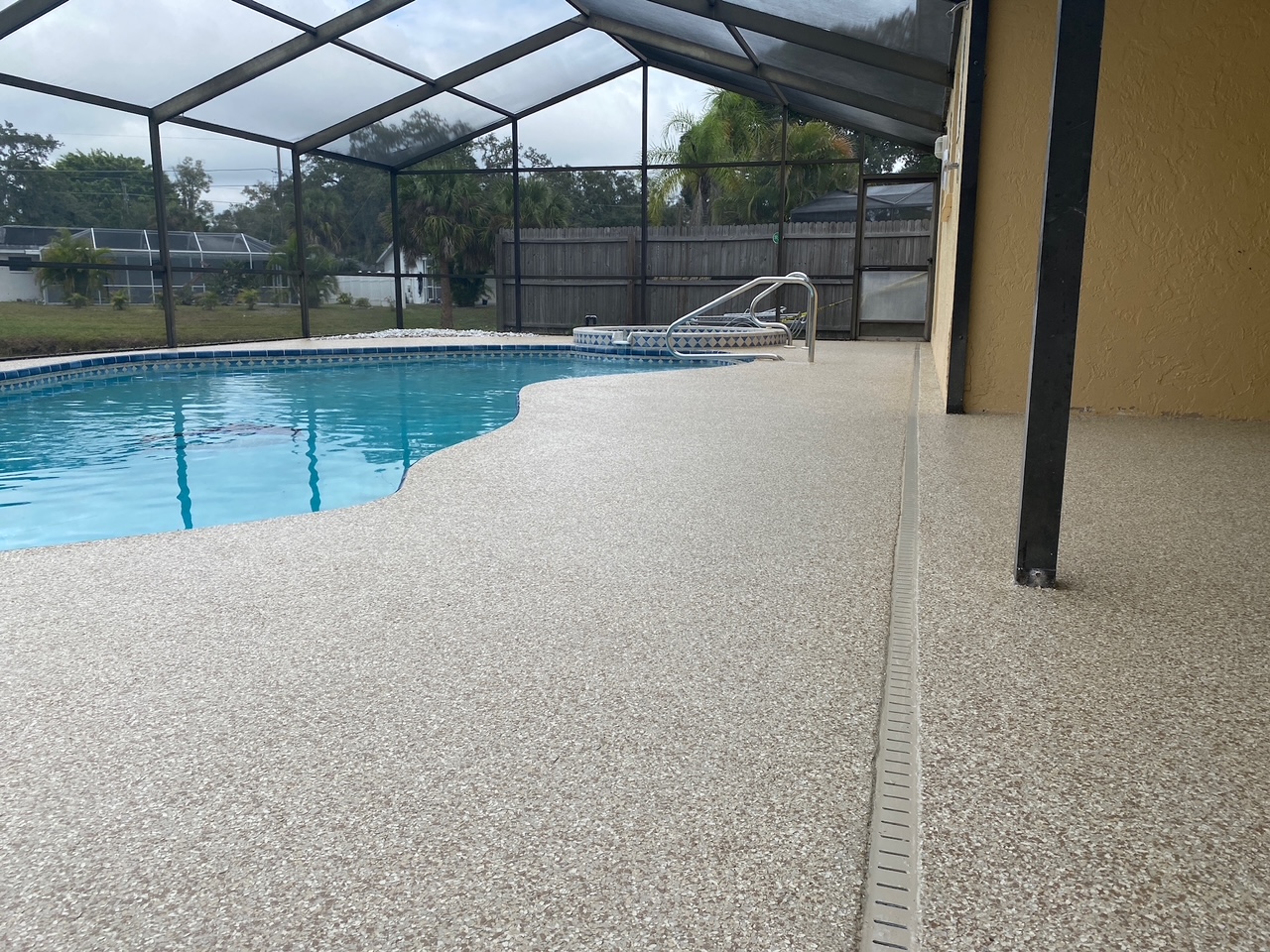 Newly refinished light flake pool deck inside a screened Florida lanai